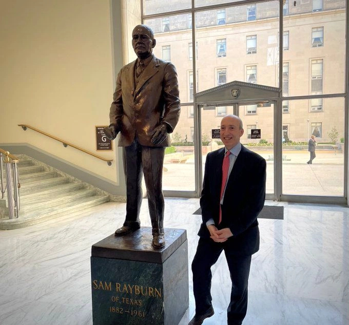 gary Gensler posing the statue of Sam Rayburn in the Rayburn House Office building